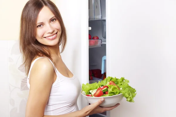 Young woman with healthy salad. background refrigerator