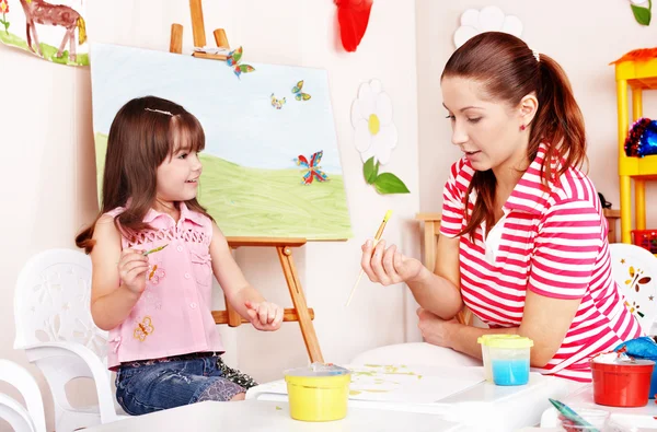 Child with teacher draw paints in play room.