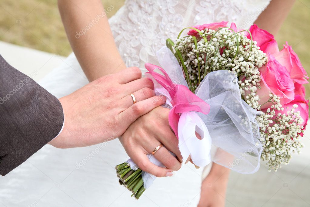 Hands and rings with wedding bouquet against a grass