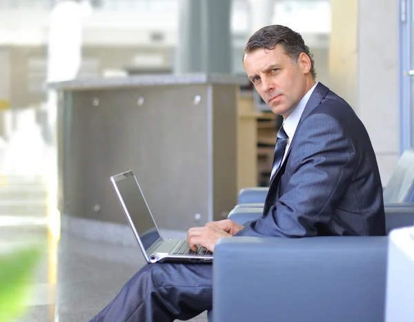 Casual looking businessman working on laptop computer in front of office wi
