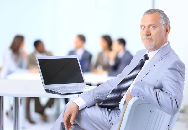 Smiling businessman using a laptop with his team in the background