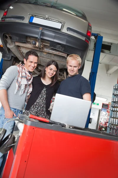 Couple standing with mechanic using laptop