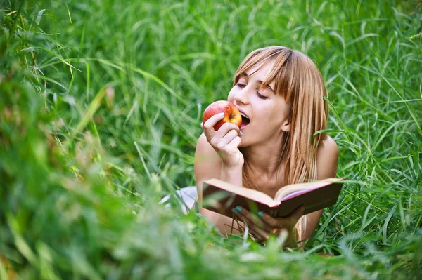 Young woman eating apple and reading book