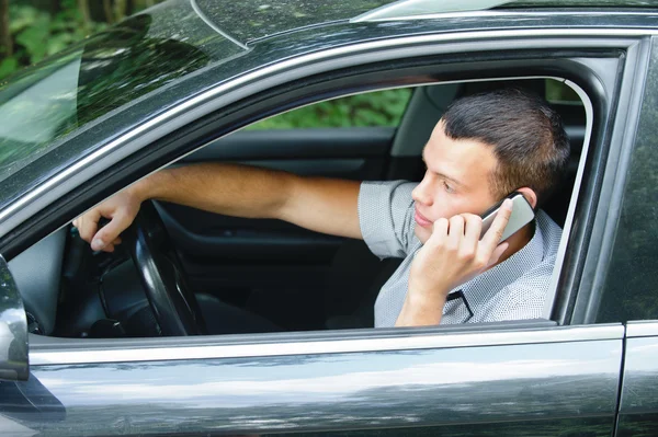 Young man speaking on telephone and driving car