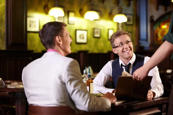 The waiter shows men in a pub menu