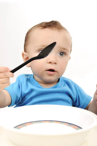 Cute adorable one year old baby with green eyes eating on table, spoon and