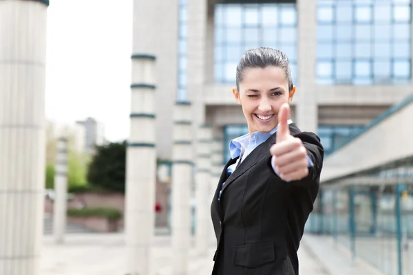 Businesswoman winking and giving thumbs up