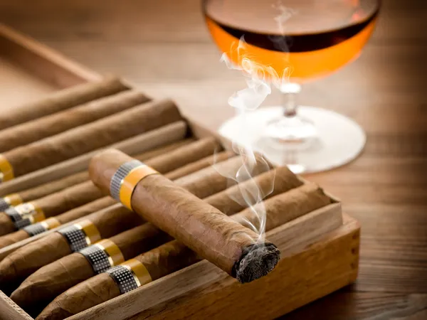 Cuban cigar and glass of liquor on wood background