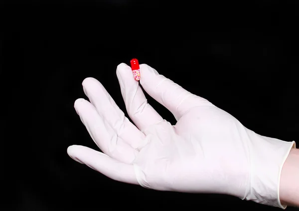 Hand holding a pill in medical gloves, on black.