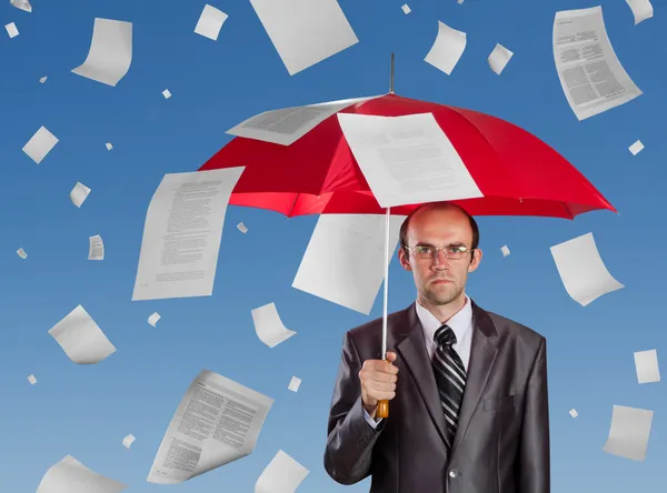 Businessman with red umbrella under falling documents
