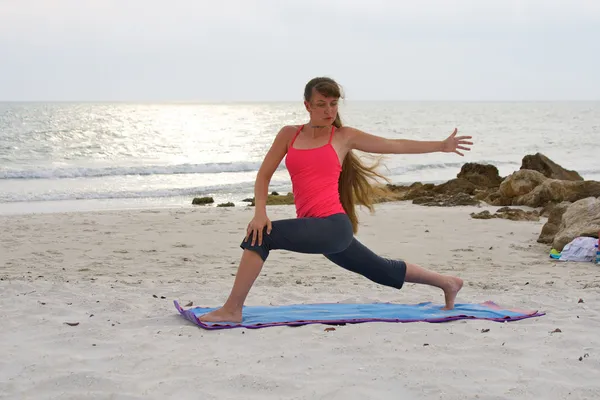 Woman on beach at sunset doing yoga exercise rotated high lunge