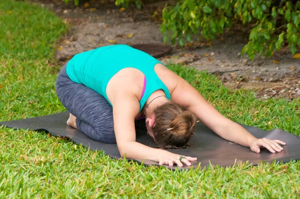 Woman doing Yoga posture Balasana or childs pose outdoors on gra