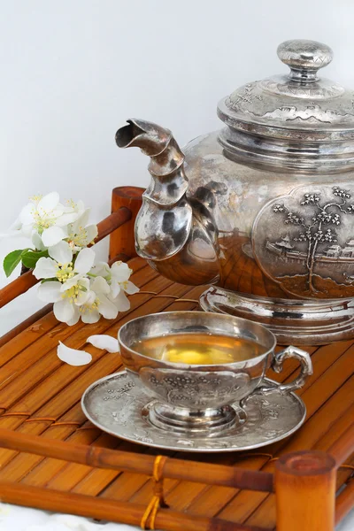 Green tea in the cup, teapot, flowers, apple trees on a bamboo t