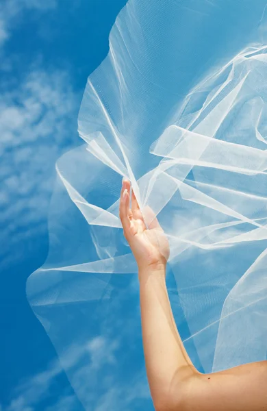Wedding dress and veil with a hand against the blue sky