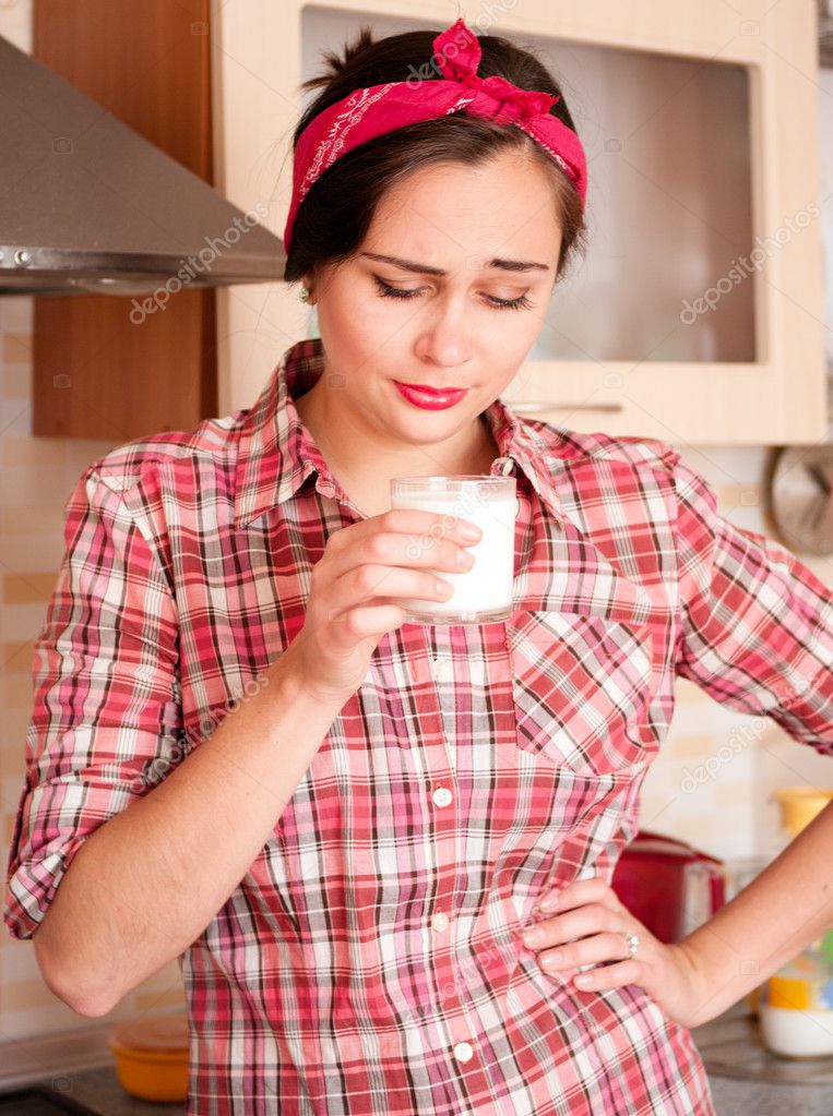 Sexy housewife in kerchief dislike glass of milk standing on the kitchen