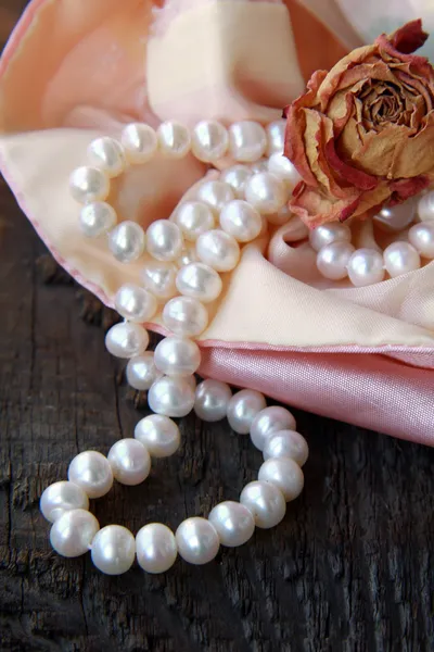 White pearls in a pink bag with dry rose