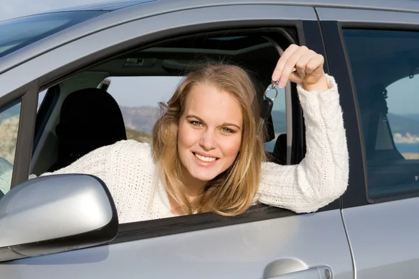 Young woman holding key to new, hire or rental car after passing, driving t
