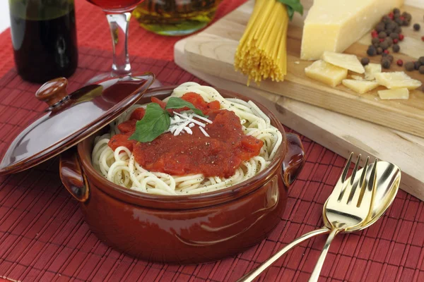 Spaghetti pasta with tomato sauce, cheese and basil in a clay pot
