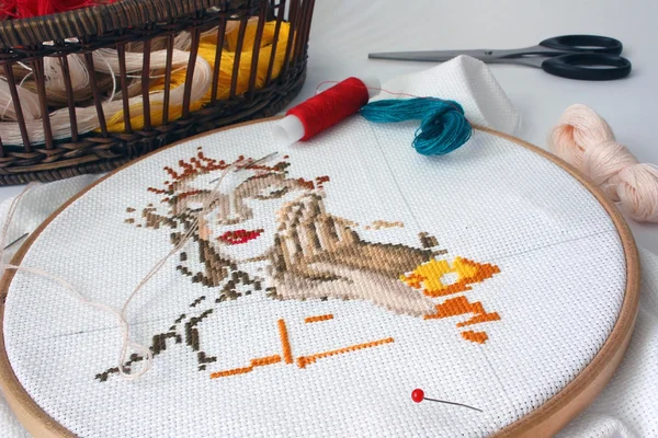 Unfinished embroidery with materials for needlework on the table