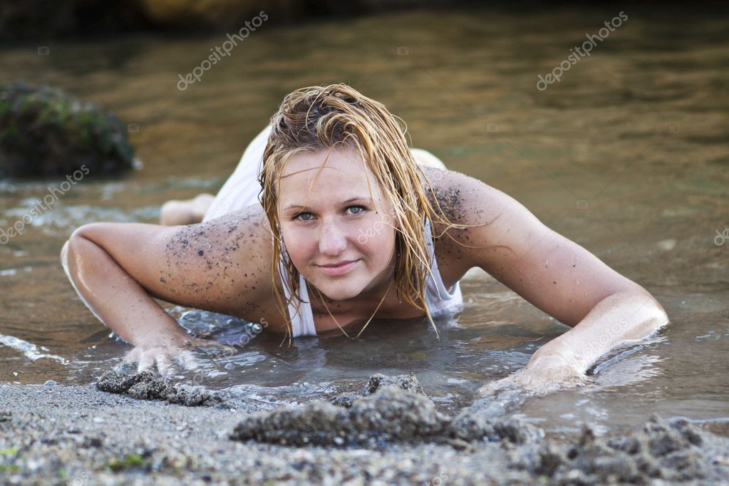 Redheaded girl in a wet white Tshirt sitting in the water and playing with