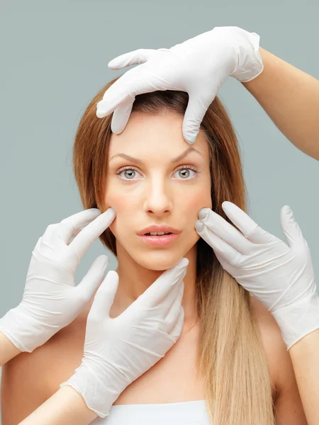 Beautiful face being examinated plastic surgeons hands