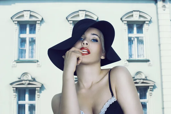 Glamour beauty wearing black hat and bra near the palace