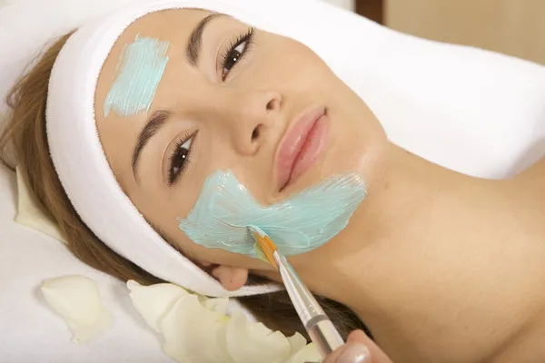 Young woman getting beauty skin mask treatment on her face with