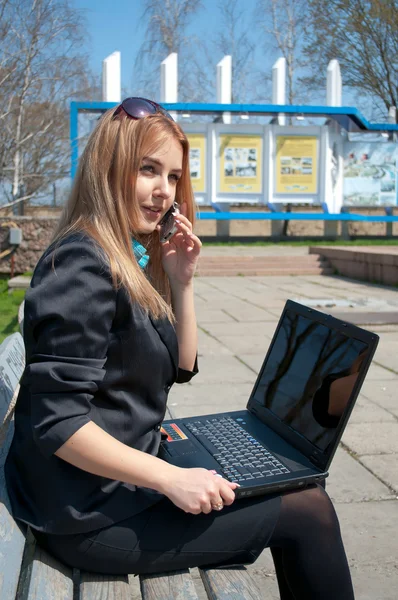 The business woman speaks by phone sitting on a bench