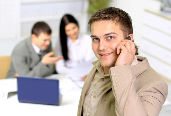 Young smiling businessman calling on phone at office