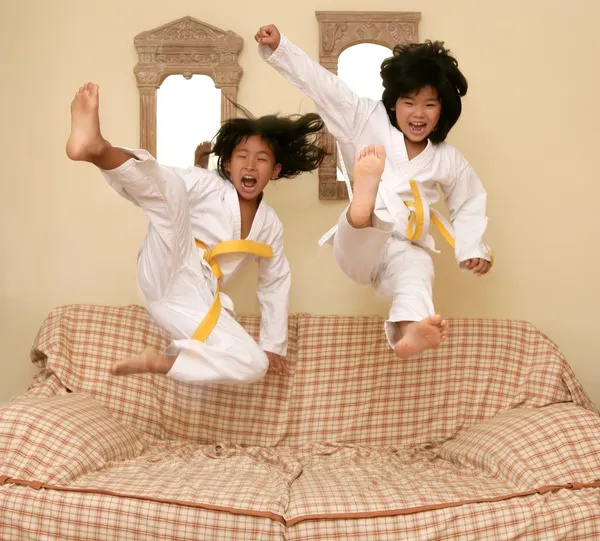 Two little asian judo gils jump on sofa