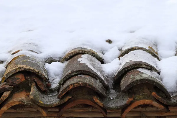 Aged clay roof tiles snowed under winter snow