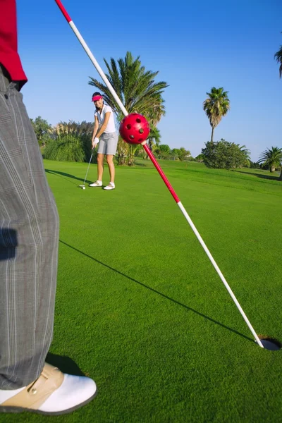Golf woman putting gol ball and man holds flag