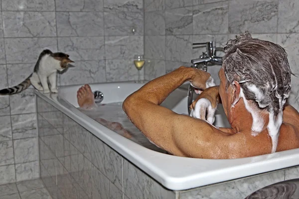 Man bathing and cat strolling around the bath tube