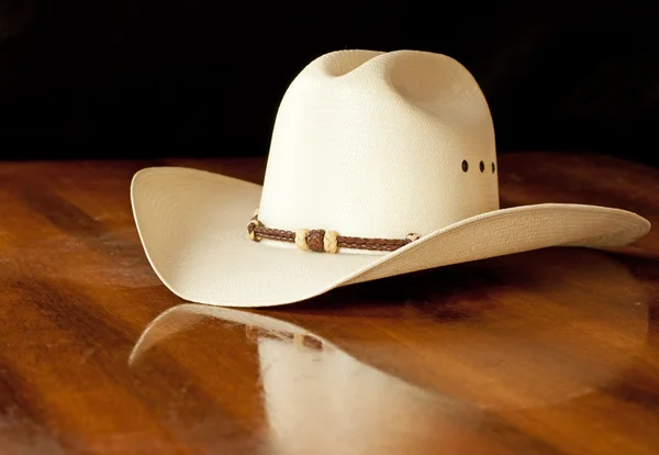 White straw cowboy hat with a hatband on a wooden table
