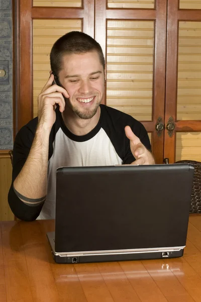 Young male on phone smiling pointing at computer