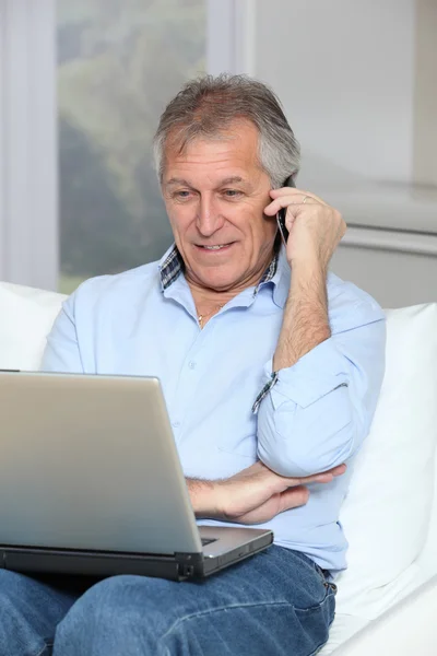 Senior man in sofa with laptop computer and mobile phone