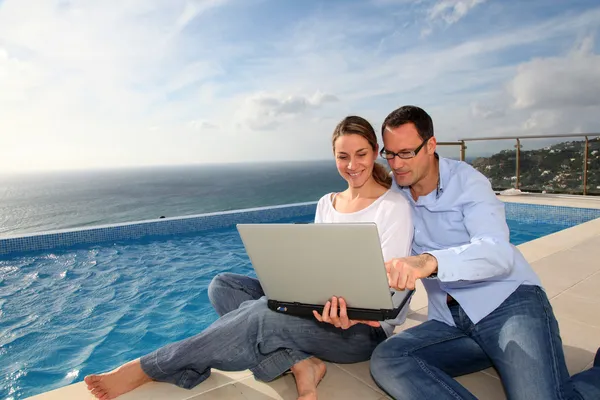 Happy couple using electronic tablet by swimming-pool