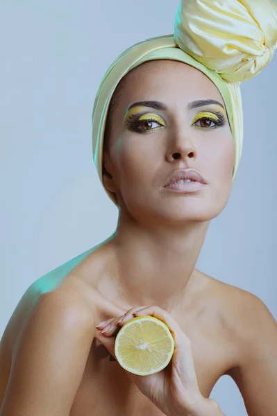 Beautiful woman with lemon in yellow scarf on her head and bright make-up