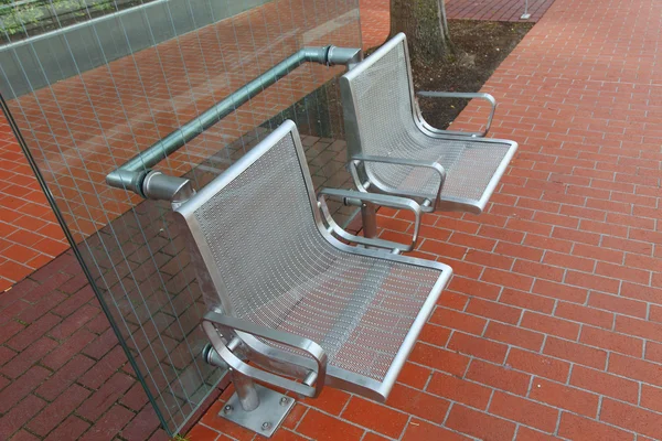 Stainless steel chairs at a bus stop.