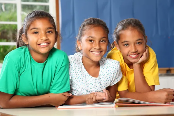 Three happy school girls reading a book in class