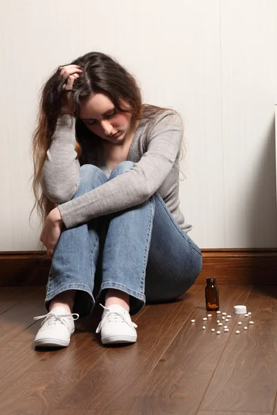 Teenage girl depressed sitting with pills on floor