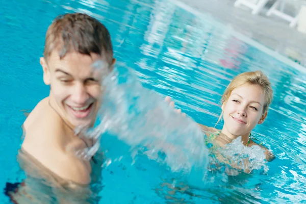 Teenage couple splashing a t the swimming pool