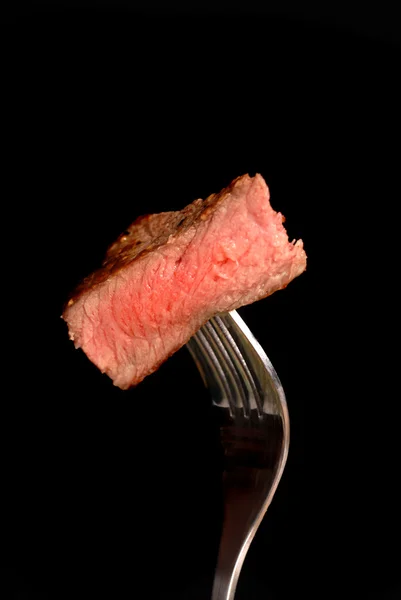 A piece of grilled ribeye steak on a fork