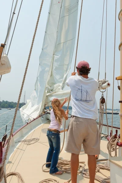 Girl helping a crew member to raise a sail.