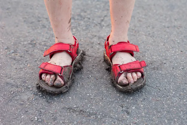 Closeup of child's dirty feet in red sandals on asphalt