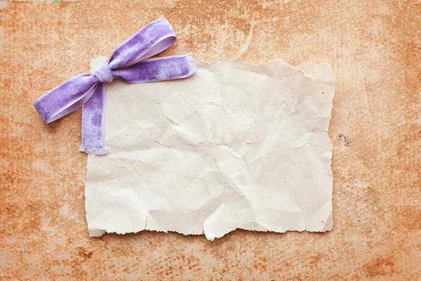 Ripped piece of paper with purple bow on grunge paper background