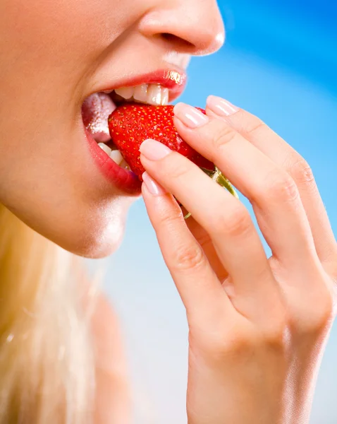 Image of young woman eating strawberry on sea beach, close-up