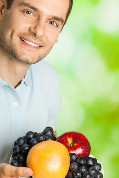 Young smiling man with plate of fruits, outdoors