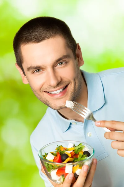 Young happy smiling man eating salad, outdoors