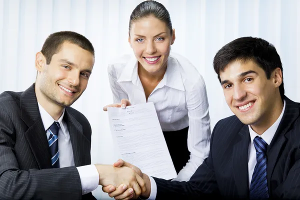 Three businesspeople handshaking with document at office